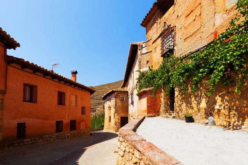Traditional Spanish village street with terracotta buildings and stone walls, typical of the country's more affordable inland regions