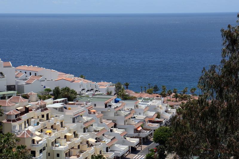 White Mediterranean-style villas and terraced apartments cascading down a steep hillside toward the deep blue Atlantic Ocean.