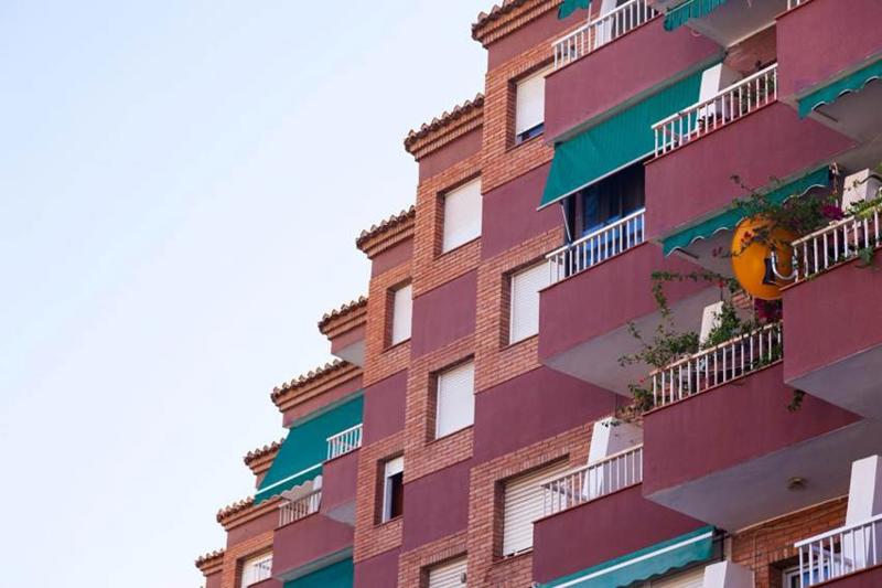 Brick apartment building in Spain with balconies, green awnings, white roller blinds and hanging plants